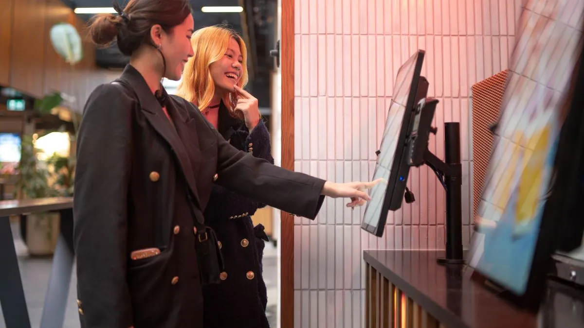 Two women putting an order for food through a kiosk