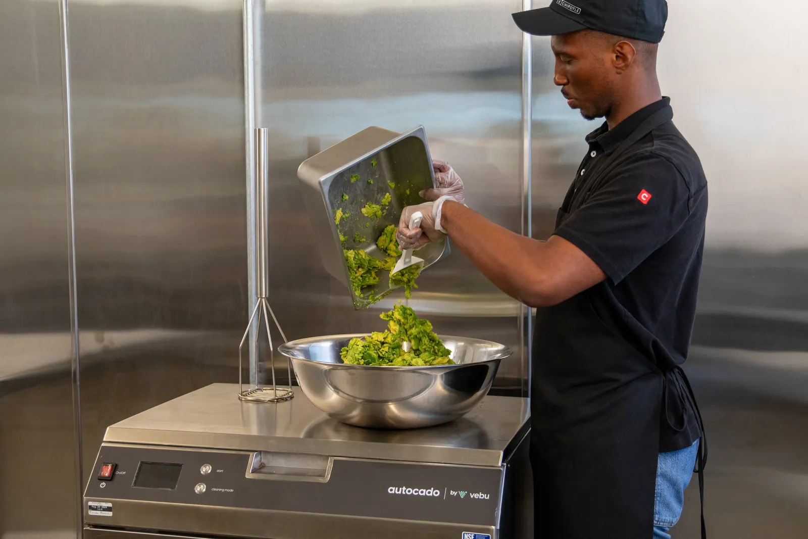 A man in a Chipotle uniform removes processed avocado from tray.