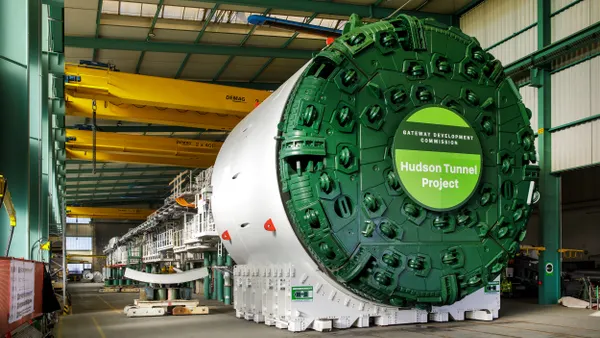 A large round machine with cutting wheels on its green face inside an industrial building.