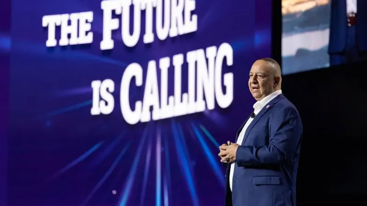 A man speaking on a keynote stage with the text to his left saying "The Future is calling"