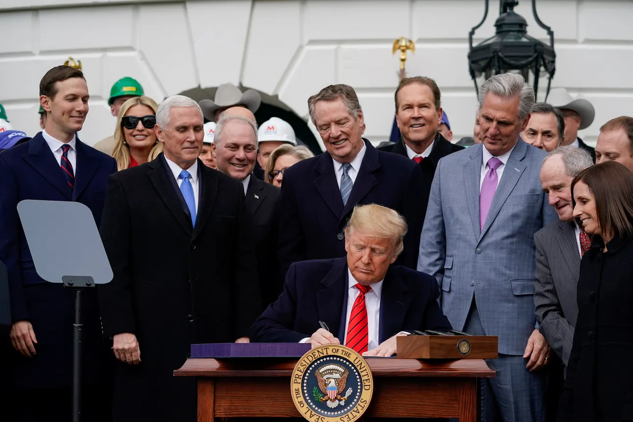 A crowd of people watches President Donald Trump sign a document