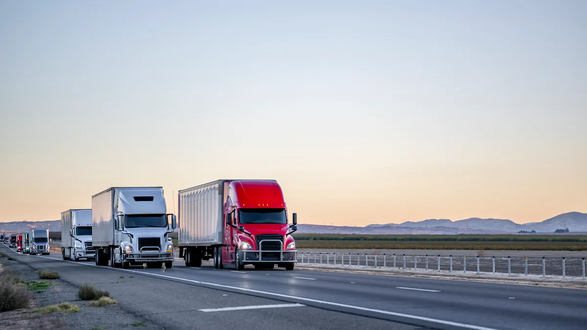 Trucks with semi trailers drive on a highway in California at twilight.