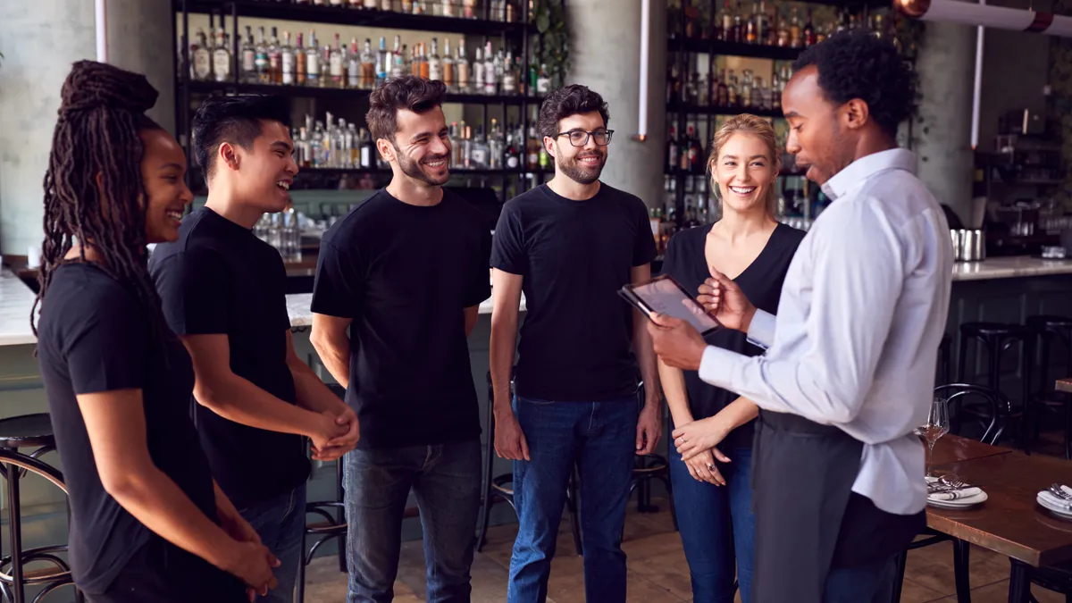 Male Restaurant Manager With Digital Tablet Giving Team Talk To Waiting Staff