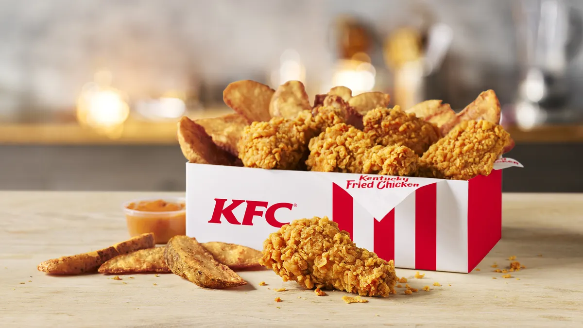 A box with potato wedges and chicken wings in it.