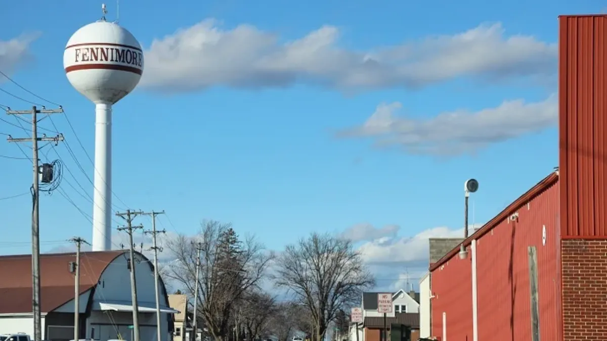 A water tower with Fennimore text on it buildings and powerlines nearby.