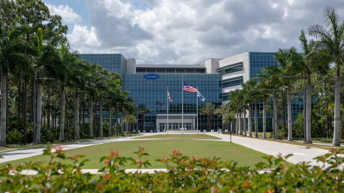 A glass building with palm trees, sidewalks and green grass in front of it.