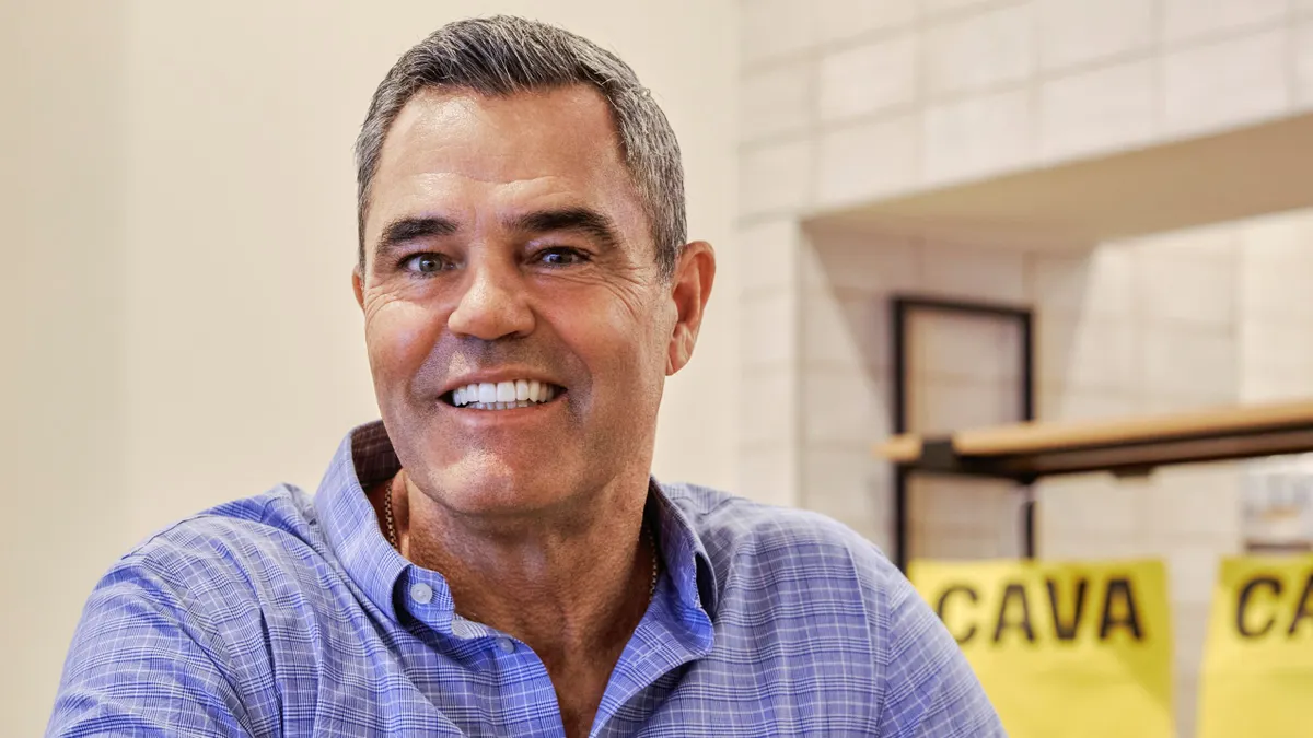 A person stands in front of a Cava logo with hands crossed.