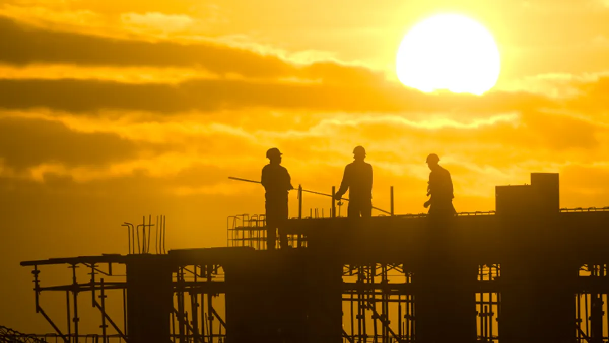 construction workers toil with the sunset in the background