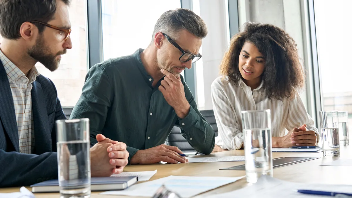 Businessman reading contract document at office table with executive team.