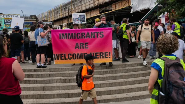 A crowd of people holding signs and a large banner that says "Immigrants Welcome Here."