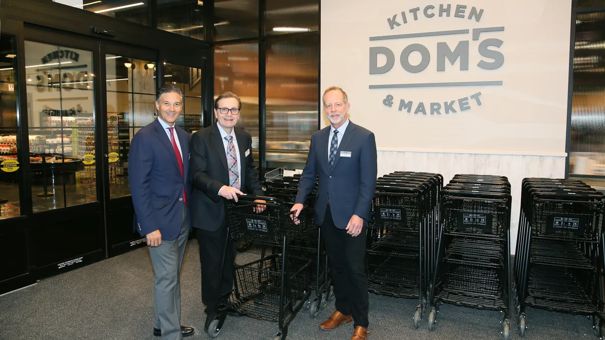 Three men standing in front of shopping carts and a sign that says Dom's Kitchen & Market.