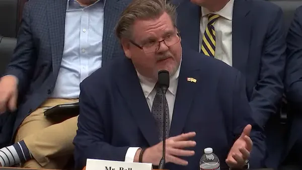 A man in a suit speaks from a desk.
