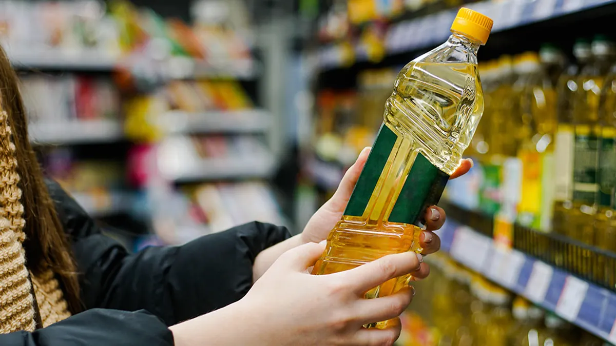 Close up of hand holding bottle of oil at store.