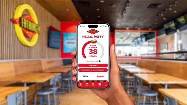 A hand holds up a smartphone with Fatburger Rewards on screen