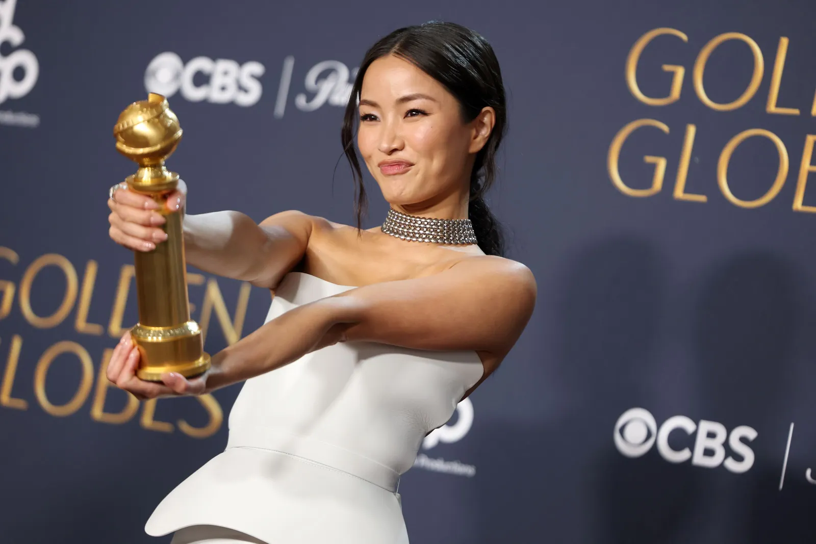 A person in a white strapless outfit holds up a Golden Globe statue.