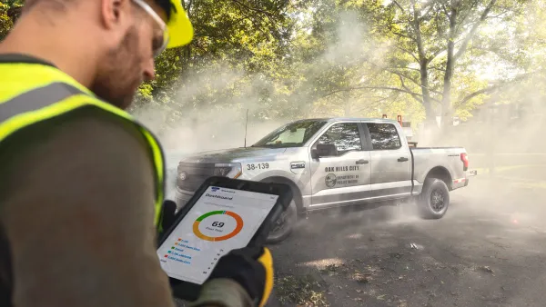 A person wearing a safety vest and helmet looks at a tablet device showing a Ford Pro dashboard with a silver F-150 pickup in the background.