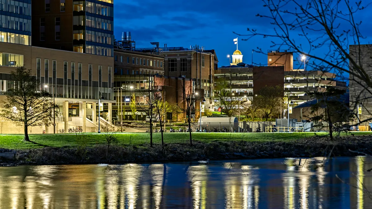 A shot at night of buildings across the other side of a river. The buildings have walkways in front of them, and green grass.