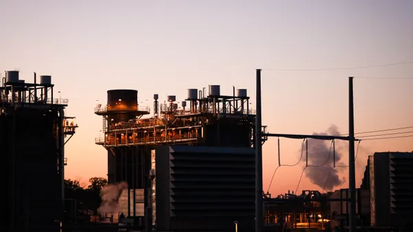 A natural gas plant is seen lit up and emitting steam at sunset.