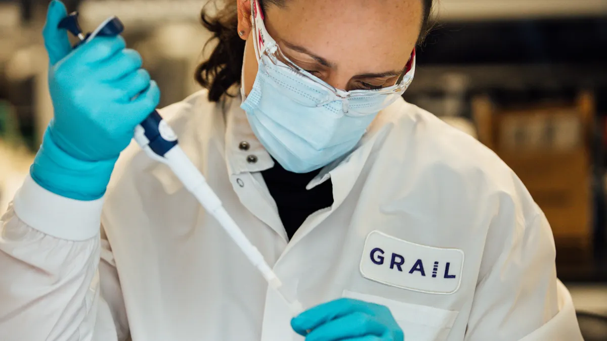 A person wearing safety goggles holds a pipette of fluid.