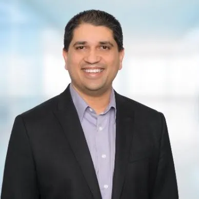 Tehsin Syed wears a black suit against a light blue background.