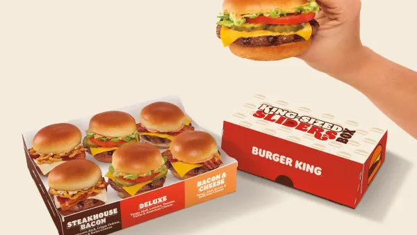 A hand holds a Burger King slider in front of boxes of similar miniature burgers.