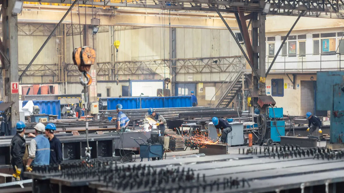 A group of people in hard hats work in a large metal processing facility