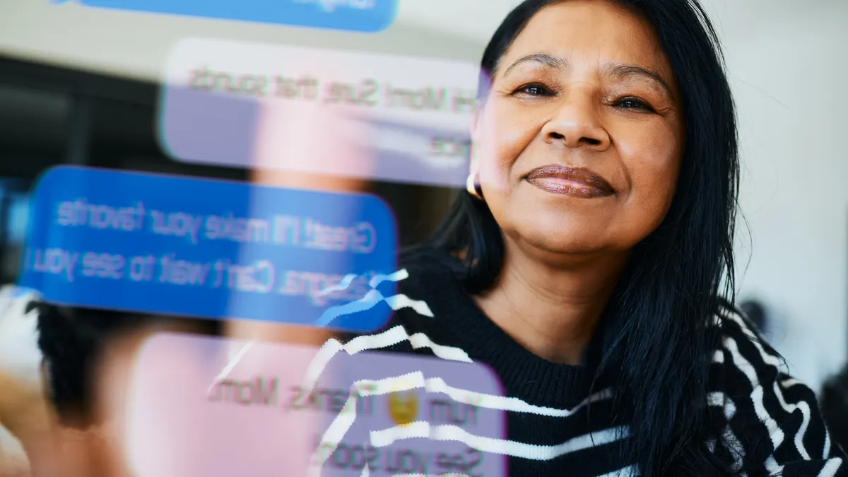 A cheerful woman of Southeast Asian descent interacts with a transparent digital screen, showing vibrant text messages in a modern well-lit environment.