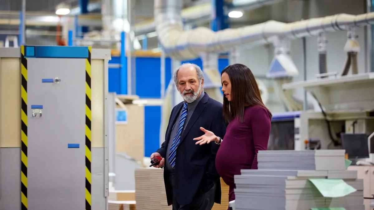 Business people, one of which is pregnant, walk and talk in afactory