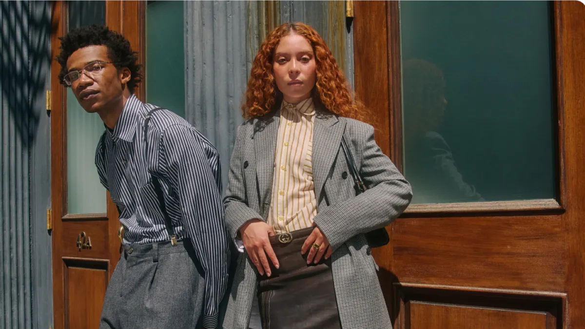Two people stand next to each other in suiting looks.