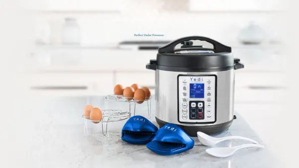 A pressure cooker on a counter next to several brown eggs, utensils and blue oven mitts.