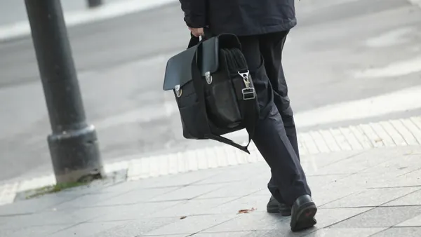 Professional dressed in formal suit and shoes carries briefcase while walking down city street