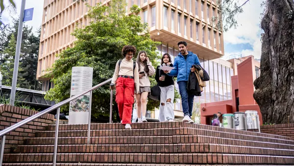 A group of college students chats while walking down stairs on campus.