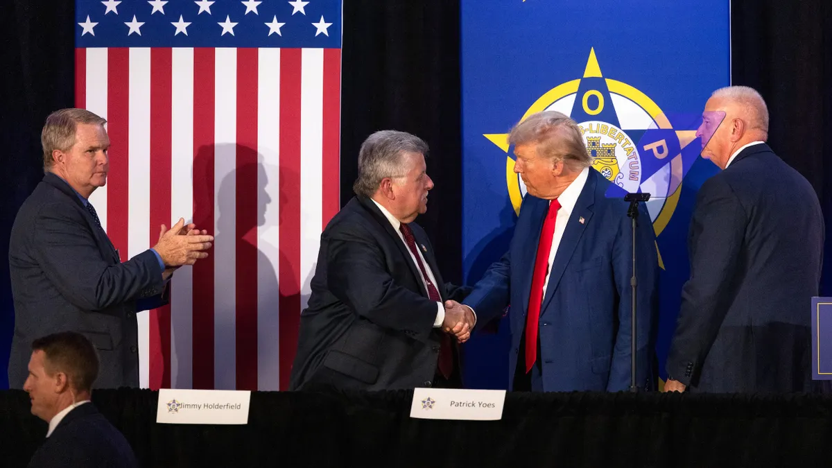 President Trump shaking hands on a stage in front of flag