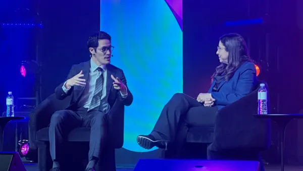 A person speaks on a stage beside another person.