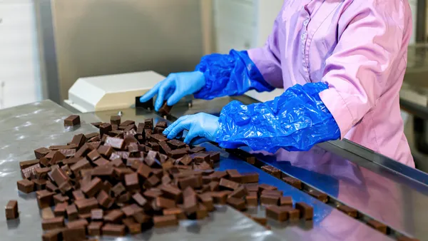 A worker in sanitary gloves handles chocolate candy in a production line.