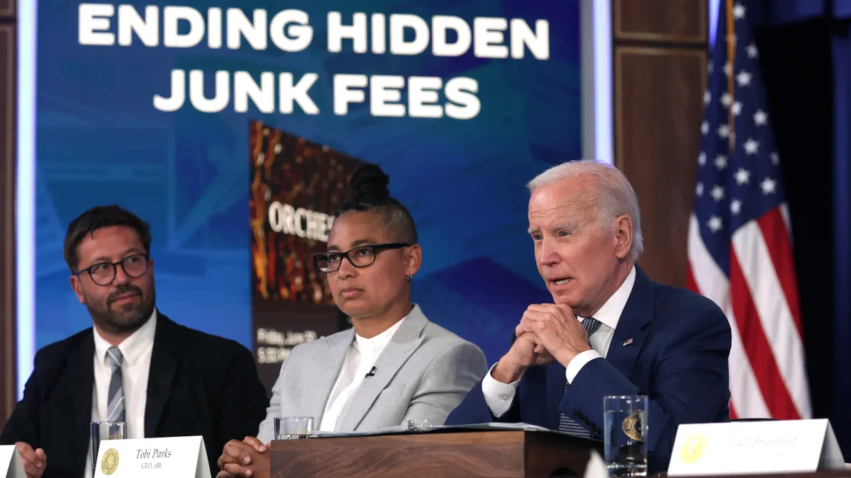 Three people sit on a panel in front of a screen that reads "Ending Hidden Junk Fees."