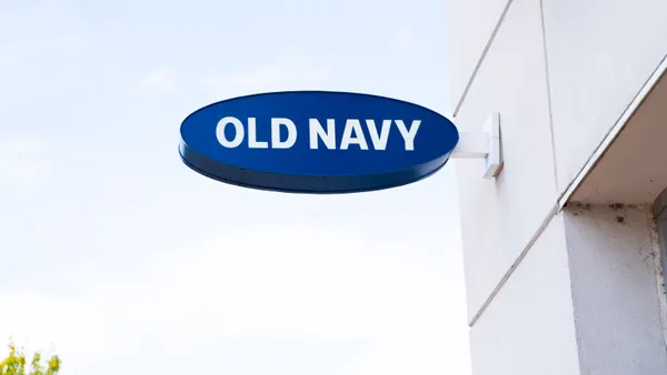 An dark blue oval sign in white capital letters spellig "Old Navy" sticks out from a white building.