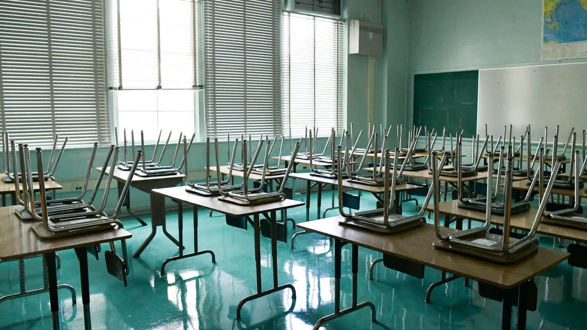 An empty classroom with stacked tables and chairs.