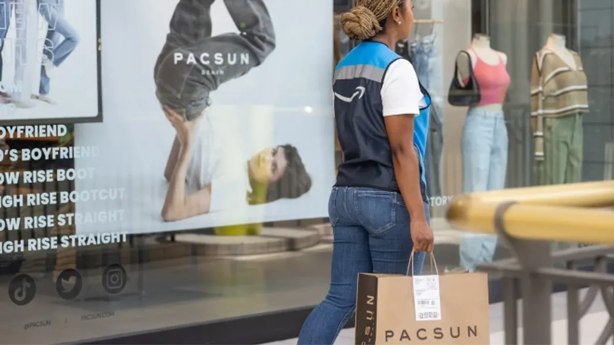 An Amazon employee walks by a Pac-Sun store window carrying a Pac-Sun bag.