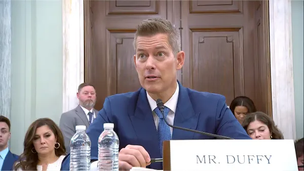 Seated man in blue suit with sign reading "Mr. Duffy."