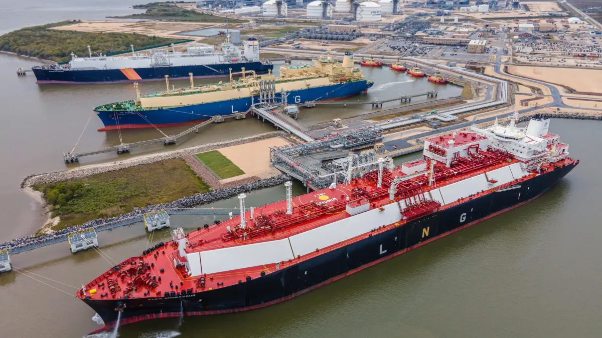 Two ships sit in an industrial harbor while an industrial facility looms in the background.