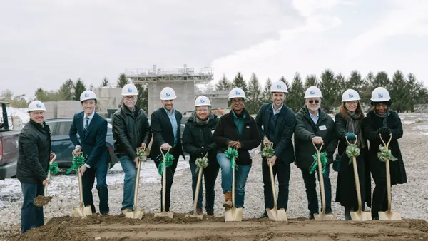 People with hard hats stand with shovels in a pile of dirt.