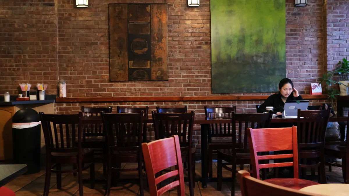 A person works on a laptop in an empty coffee shop.