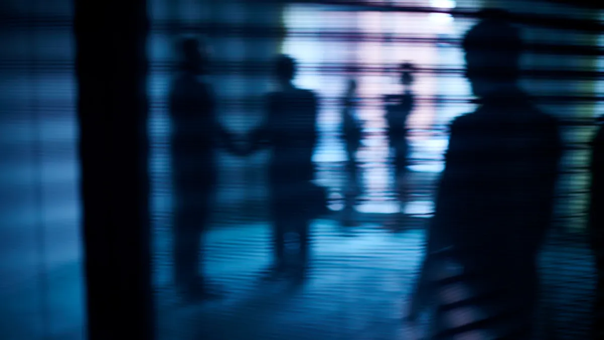 Silhouettes of business people interacting behind window with blinds
