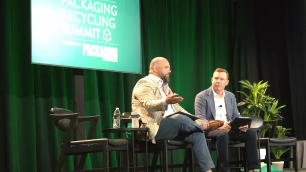 Two people sit in chairs on a stage in front of a green background that says Packaging Recycling Summit.