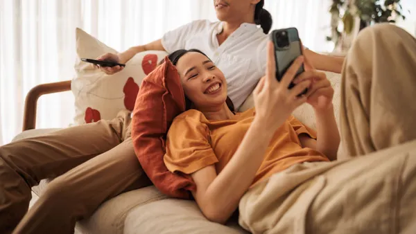 A person checks their phone while leaning on their partner on a living room couch