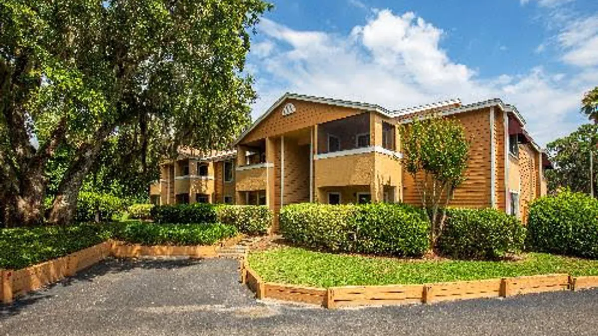 Brown apartment building with trees and shrubs in the foreground.