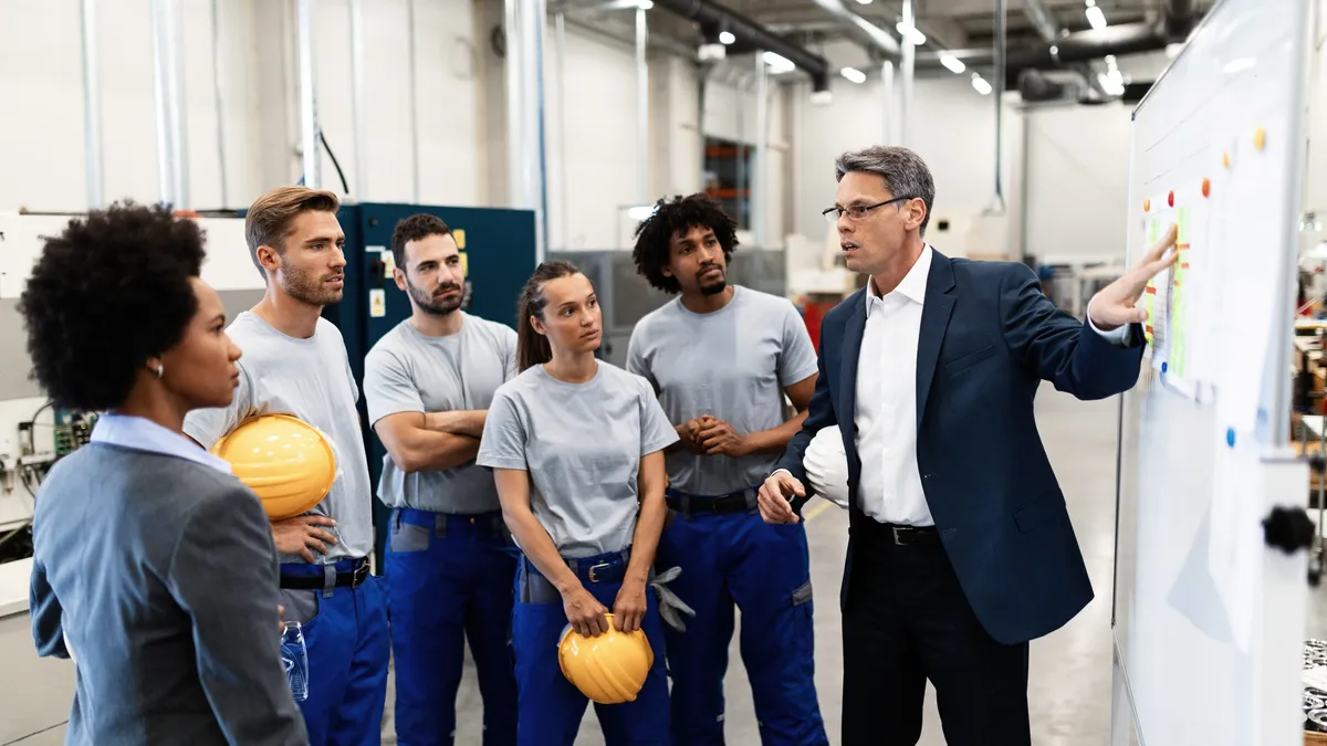 A corporate manager gives a presentation to a team of factory workers.