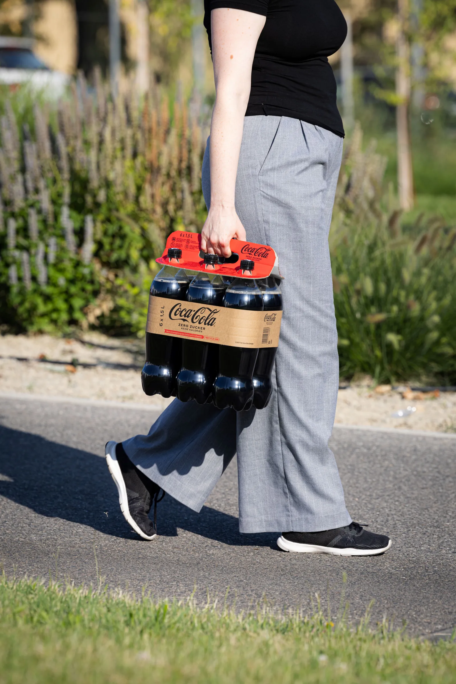 A person carries a multi-pack of 1.5 liter PET Coca-Cola soft drink bottles using a recyclable corrugated cardboard handle from DS Smith called Lift Up.