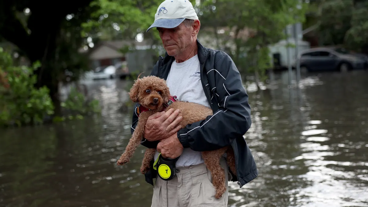A person holding a small dog walks in a flooded street.